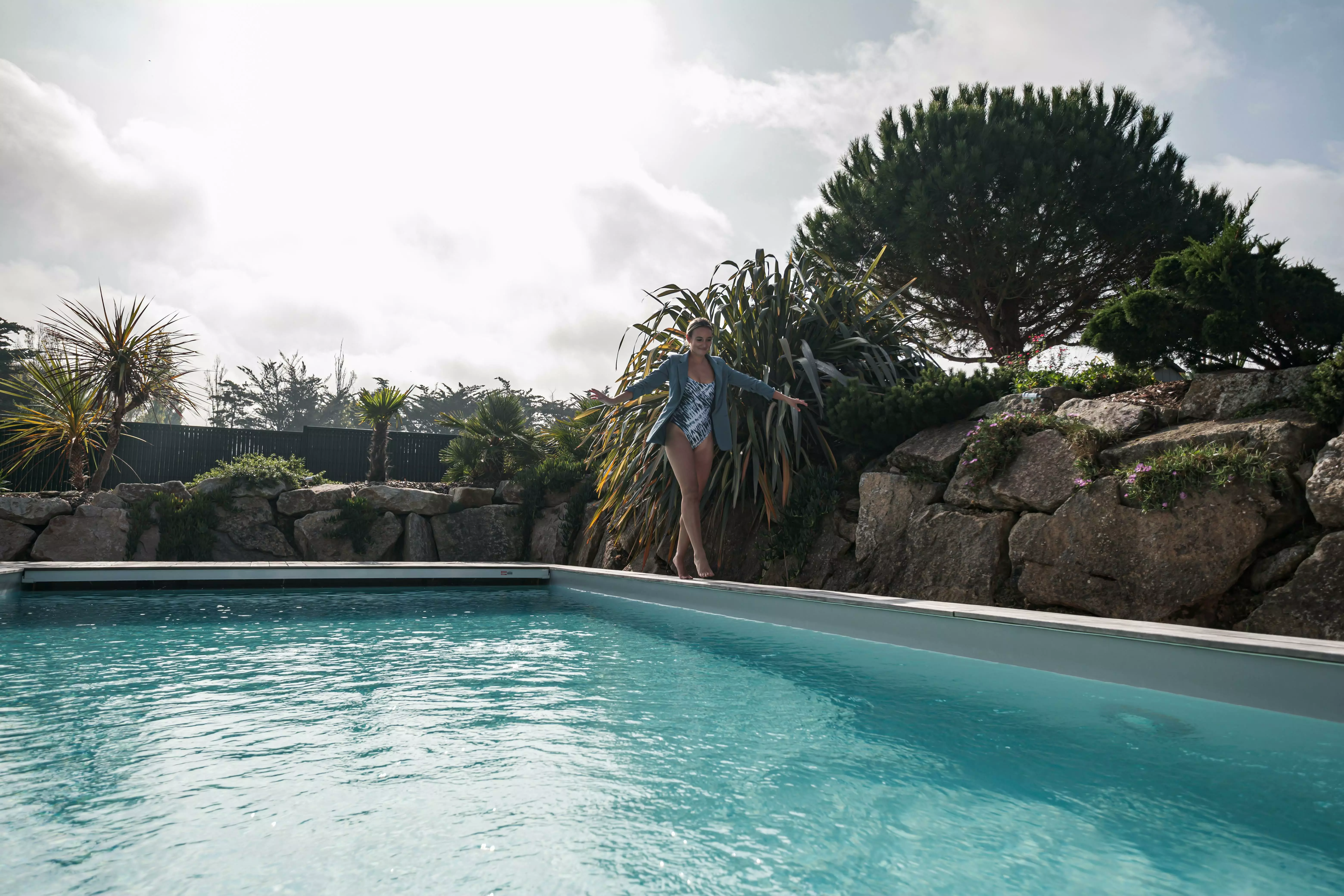 Une maison d'aujourd'hui, avec la piscine en son centre, juxtaposée à un ensemble rocheux par une terrasse, et agrémentée de flore exotique.