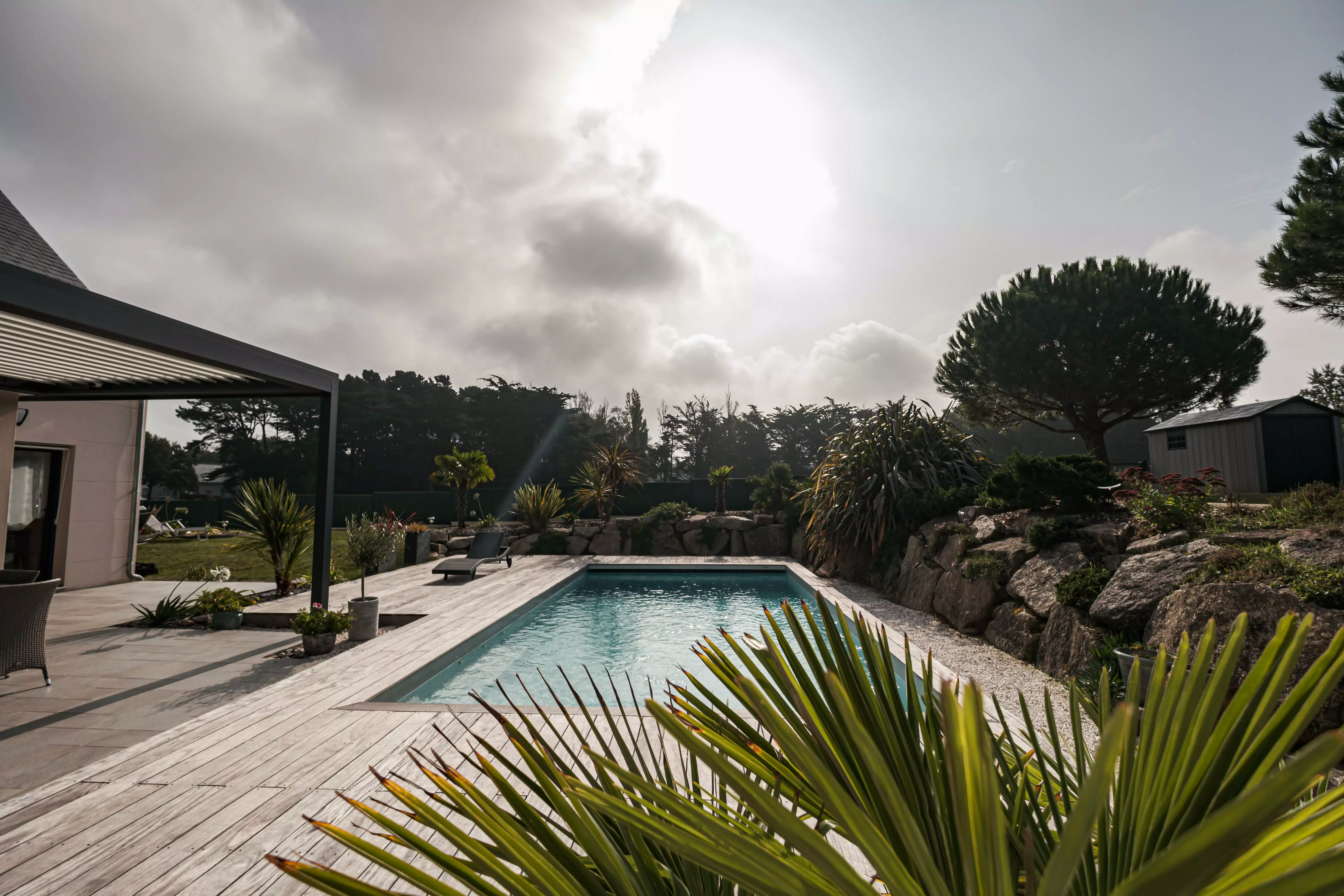 Une maison d'aujourd'hui où la piscine joue le rôle principal, connectée via une terrasse à un cadre rocheux étoffé de plantes venues d'ailleurs.