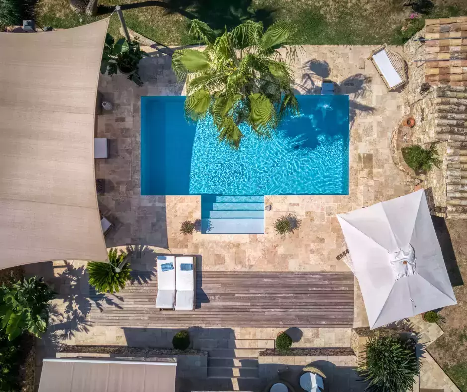 Transition d'une piscine coque vers une piscine en maçonnerie, complétée par un palmier exotique, un point d'eau et une plateforme en travertin.